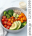 vibrant and healthy bowl featuring roasted sweet potatoes, cherry tomatoes, broccoli, quinoa, and avocado, drizzled with creamy dressing 123651099