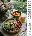 Fresh salad with tomatoes, avocado, and bread on table with flowers and juice. vibrant and healthy meal surrounded by nature beauty 123651102