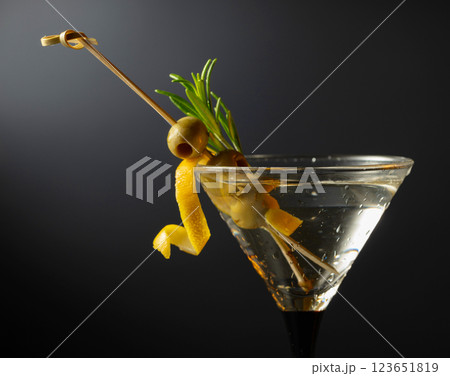 Classic dry martini cocktail with green olives, lemon peel, and rosemary on a black background. Classic dry martini cocktail with green olives, lemon peel, and rosemary on a black background. 123651819