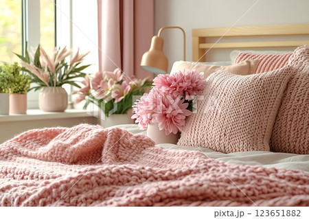 Cozy bedroom with knitted pink pillows, a soft blanket, and fresh flowers in a vase on a sunny morning Cozy bedroom with knitted pink pillows, a soft blanket, and fresh flowers in a vase on a sunny morning 123651882