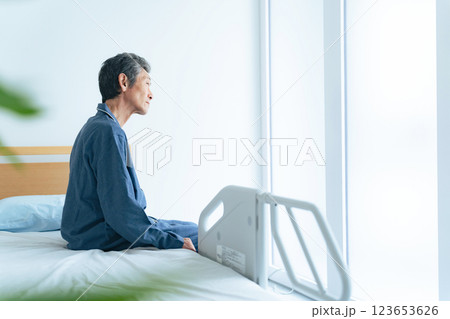 ベッドに座ってぼんやり外を眺めるシニア男性 123653626