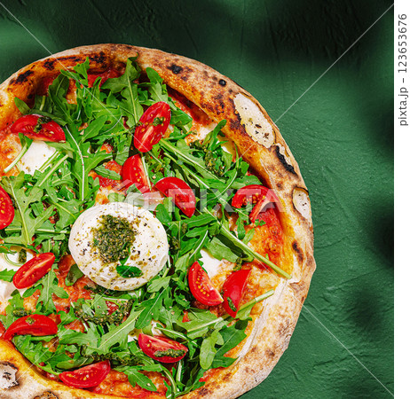 Fresh pizza topped with arugula and cherry tomatoes on a green table 123653676