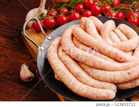 Fresh sausages prepared for grilling with herbs and tomatoes 123653712