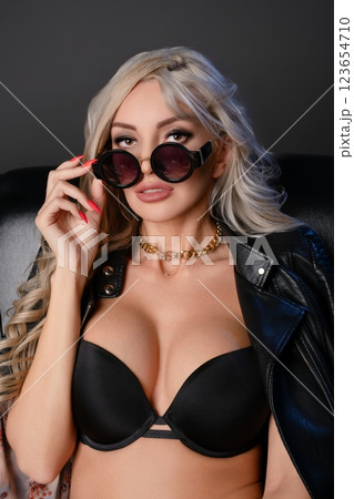 Confident woman in stylish lingerie and sunglasses poses on a leather chair 123654710