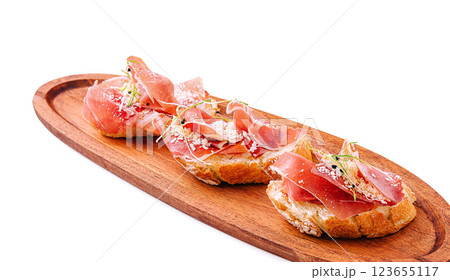 Delicious bruschetta topped with prosciutto and herbs on wooden board 123655117
