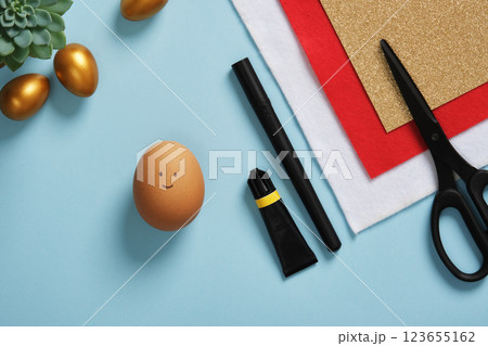 A DIY Easter egg with a smiling face on a background of art supplies. Crafting accessories. A DIY Easter egg with a smiling face on a background of art supplies. Crafting accessories. 123655162