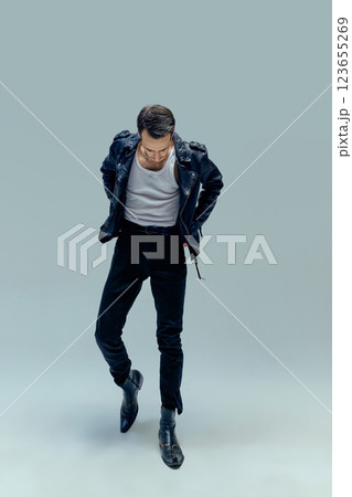 Introspective young man,musical artist, posing looking down while adjusting his leather jacket against gradient background. Concept of vintage, rock, attitude, charisma. Introspective young man,musical artist, posing looking down while adjusting his leather jacket against gradient background. Concept of vintage, rock, attitude, charisma. 123655269
