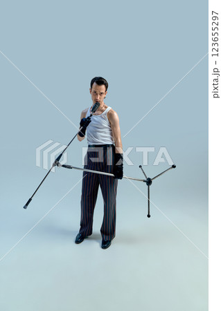Young singer gripping microphone stand with intense focus, exuding timeless stage confidence against gradient studio setting. Vintage charisma. Young singer gripping microphone stand with intense focus, exuding timeless stage confidence against gradient studio setting. Vintage charisma. 123655297