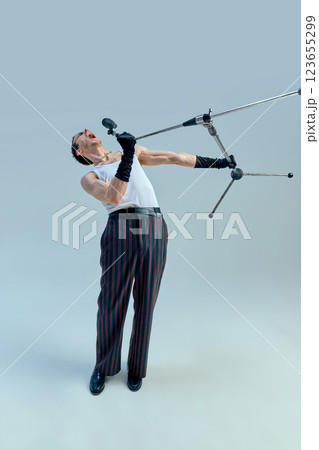 Talented vocalist pushing boundaries, microphone stand twisting mid-air in dramatic moment of musical expression against studio backdrop. Talented vocalist pushing boundaries, microphone stand twisting mid-air in dramatic moment of musical expression against studio backdrop. 123655299