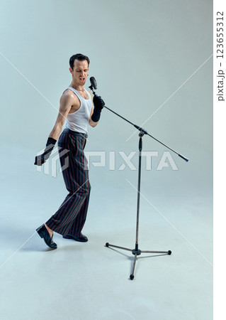 Rhythmic tension embodied in angular stance, artist fully immersed in musical expression, microphone extension of electric performance against white background. 123655312