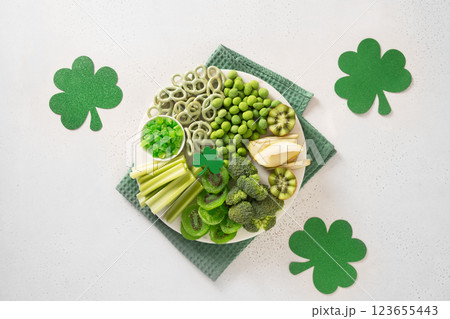St. Patrick's Day Inspired Snacks charcuterie board and traditional party decorations, green clover leaves on white background. Festive holiday appetizer. Top view St. Patrick's Day Inspired Snacks charcuterie board and traditional party decorations, green clover leaves on white background. Festive holiday appetizer. Top view 123655443