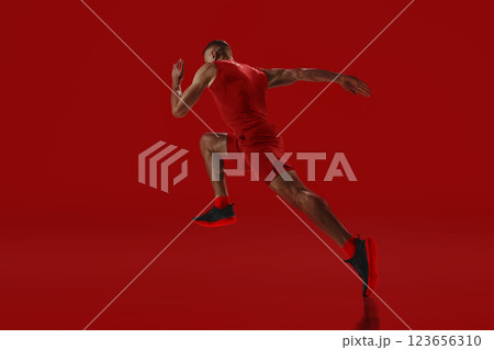 Dynamic composition. Sprinter in red accelerating into motion, power and agility radiating against vivid background. Concept of sport 123656310
