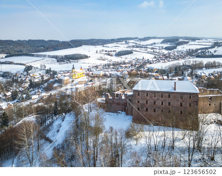 Snow covers the medieval Pecka castle, standing proudly amidst a picturesque winter landscape in Czechia. Nearby, a quaint village and rolling hills add to the serene scenery. 123656502