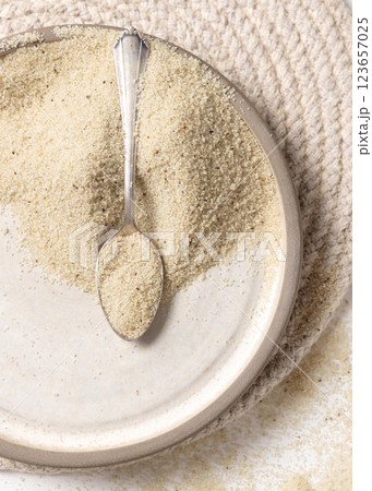 Raw uncooked fonio seeds on a plate with a metal spoon on white table. African ancient pseudocereal Raw uncooked fonio seeds on a plate with a metal spoon on white table. African ancient pseudocereal 123657025