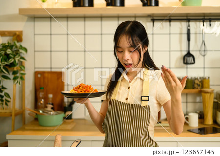 Young woman holding a freshly prepared plate of spaghetti with tomato sauce in her kitchen 123657145