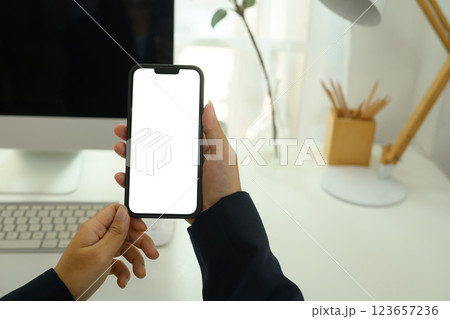 Close up of businessperson holding smartphone with white screen sitting at desk 123657236