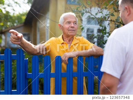 Neighbor conversation. Two smiling men breezily chatting near fence of rural house 123657348