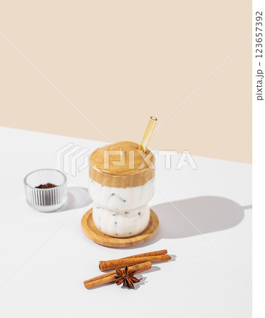 Korean whipped drink Dalgona coffee in a glass on a white beige background with spices and shadow. Korean whipped drink Dalgona coffee in a glass on a white beige background with spices and shadow. 123657392