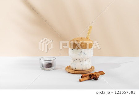 Korean whipped drink Dalgona coffee in a glass on a white beige background with spices and shadow. 123657393