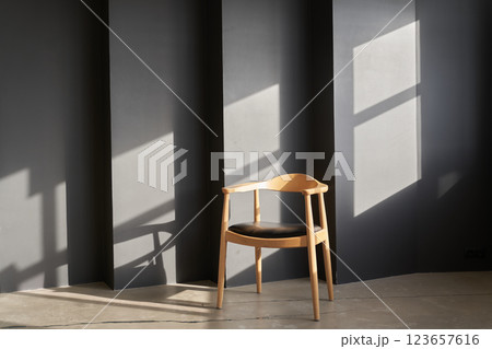 There is sunlight on the black uneven wall. With space to copy. A wooden chair with a rounded shape and design stands against a dark wall. High quality photo There is sunlight on the black uneven wall. With space to copy. A wooden chair with a rounded shape and design stands against a dark wall. High quality photo 123657616