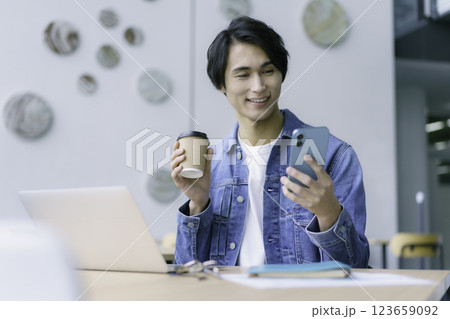 スマホとコーヒーを手にpc作業をする若い男性　撮影協力:スカパー東京メディアセンター 123659092