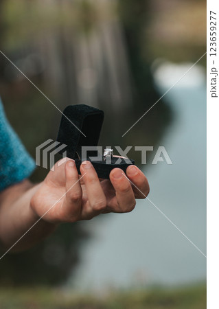 Close up of man hands holding engagement ring box on the beach Close up of man hands holding engagement ring box on the beach 123659277