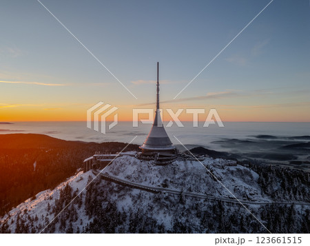 The first light of day breaks over Jested Mountain, illuminating the snowy peak and surrounding forest. A serene winter scene captured at sunrise, showcasing nature's quiet beauty. 123661515