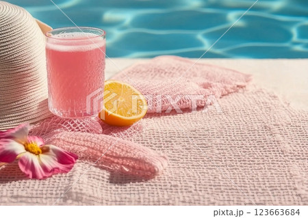 A glass filled with pink beverage decorated with a hat, pink towel, a mesh bag on the scarf. Concept of recovery, sun protection and moisturizing product with vacant space 123663684