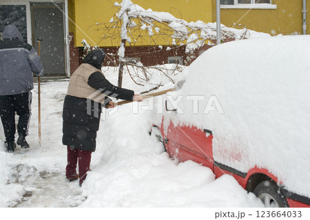 Senior Shoveling Snow from Parked Car in Residential Area 123664033