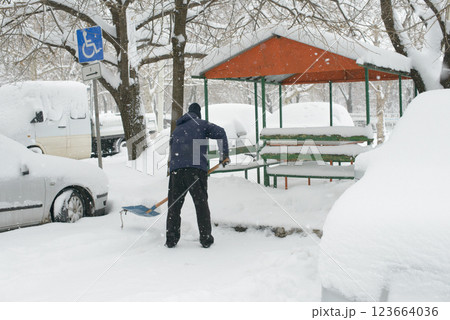 Man Clearing Snow from Handicapped Parking Space Near Park Bench Man Clearing Snow from Handicapped Parking Space Near Park Bench 123664036