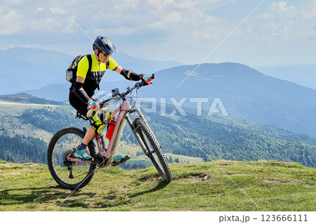 Cyclist man riding electric mountain bike outdoors. Male tourist biking along grassy trail in the mountains, wearing helmet and backpack. Concept of sport, active leisure and nature. Cyclist man riding electric mountain bike outdoors. Male tourist biking along grassy trail in the mountains, wearing helmet and backpack. Concept of sport, active leisure and nature. 123666111