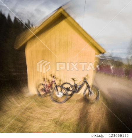 Two modern electric mountain bikes leaning to small wooden house (no people). Motion blur. 123666153
