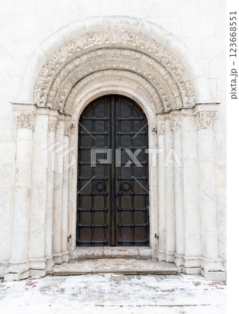 An old black metal door is in white wall of an ancient church, front view 123668551