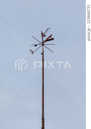 A weather vane mounted on a tall metal pole under a serene blue sky 123668731