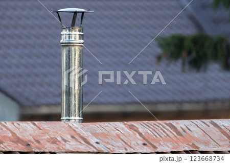 A metallic chimney pipe with a cap stands on a red roof 123668734