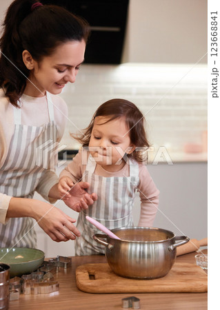 mother and her little child daughter in aprons preparing the dough in the kitchen, bake cookies 123668841