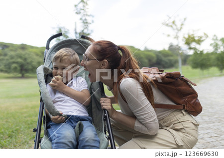 Mother having fun while talking to her toddler sitting in a stroller in a park Mother having fun while talking to her toddler sitting in a stroller in a park 123669630