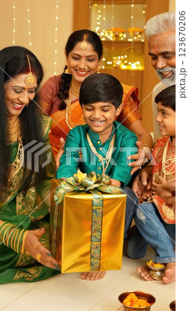 Indian family, dressed in traditional attire, gives wrapped presents to a delighted child during the diwali festival celebration in a decorated home setting Indian family, dressed in traditional attire, gives wrapped presents to a delighted child during the diwali festival celebration in a decorated home setting 123670206