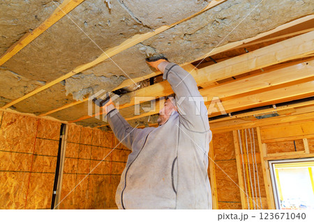 Worker installs insulation in new home, on ceilings for better energy efficiency during renovations Worker installs insulation in new home, on ceilings for better energy efficiency during renovations 123671040