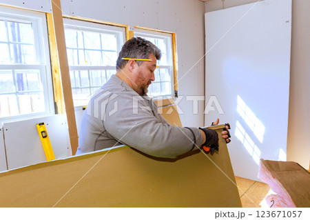 Worker measures cuts drywall in sunlit room, showcasing craftsmanship during renovation efforts. 123671057