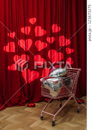 supermarket trolley full of foil balloons on red background. creative photo zone with hearts 123673275