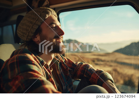Content young man with a beanie hat smiles serenely while on a road trip, taking in the scenic desert landscape from his camper van 123674094