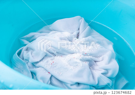 Hand laundry washing clothes in blue plastic basin with detergent powder and oxygen bleach Hand laundry washing clothes in blue plastic basin with detergent powder and oxygen bleach 123674682