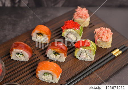 Set of sushi roll with caviar, avocado, tuna, salmon; chopsticks on wooden serving board.. Dark black texture background with copy space. Close up. Japan menu. Asian food Set of sushi roll with caviar, avocado, tuna, salmon; chopsticks on wooden serving board.. Dark black texture background with copy space. Close up. Japan menu. Asian food 123675931