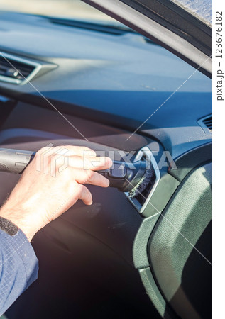 Close-up of hand cleaning car interior air vent with a vacuum attachment. High quality photo 123676182