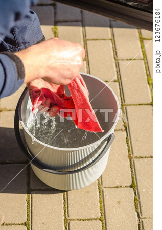 Man Squeeze Water from hands and washing wipe into Bucket Outdoors on Sunny Day. High quality photo Man Squeeze Water from hands and washing wipe into Bucket Outdoors on Sunny Day. High quality photo 123676184