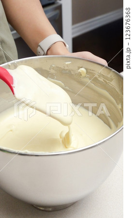 Close-Up of a Person Mixing Thick and Creamy Batter in a Stainless Steel Bowl with a Red Spatula 123676368