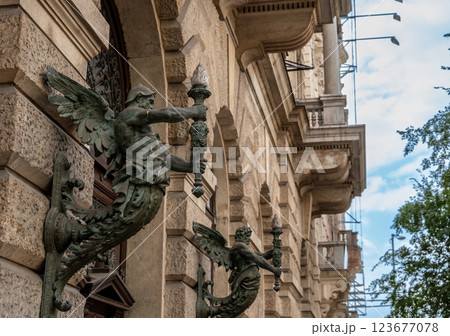 Budapest,Hungary,August 30,2022. Street view with a detail of two street lamps on the facade of a historic building in the historic center. They are made of metal statues of human features with wings. 123677078