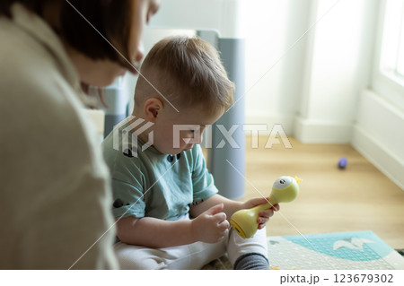 The child is sitting calmly playing with a toy, next to his mother 123679302