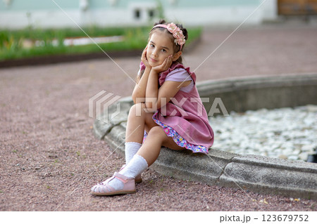 Young caucasian girl in pink dress sitting by fountain in garden Young caucasian girl in pink dress sitting by fountain in garden 123679752